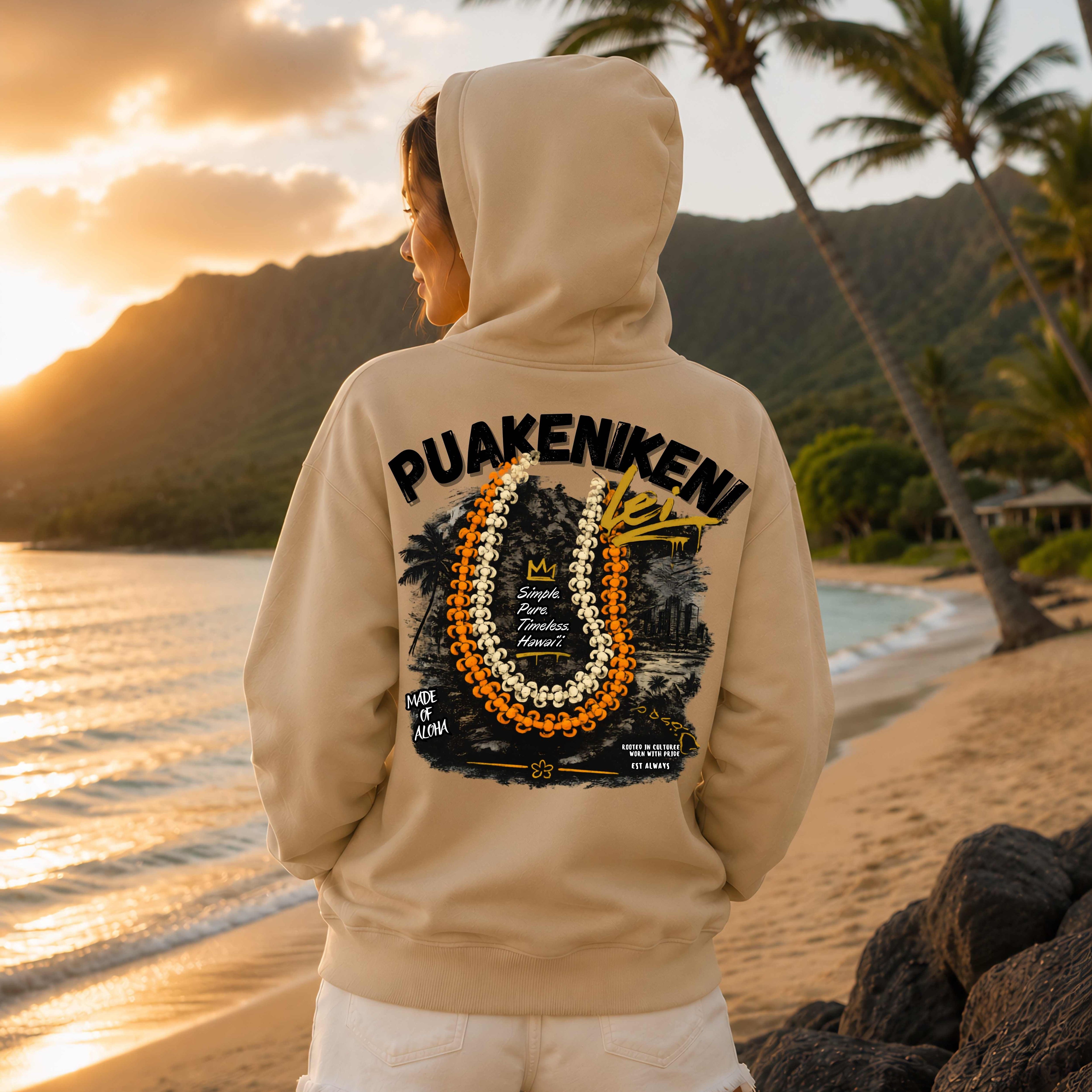 Person wearing a beige hoodie with 'PUAKENIKENI' design with a Background of Waikiki  on a beach at sunset