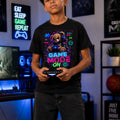 Person wearing a black t-shirt with a colorful graphic and text, holding a gaming controller in a room with gaming decor.
