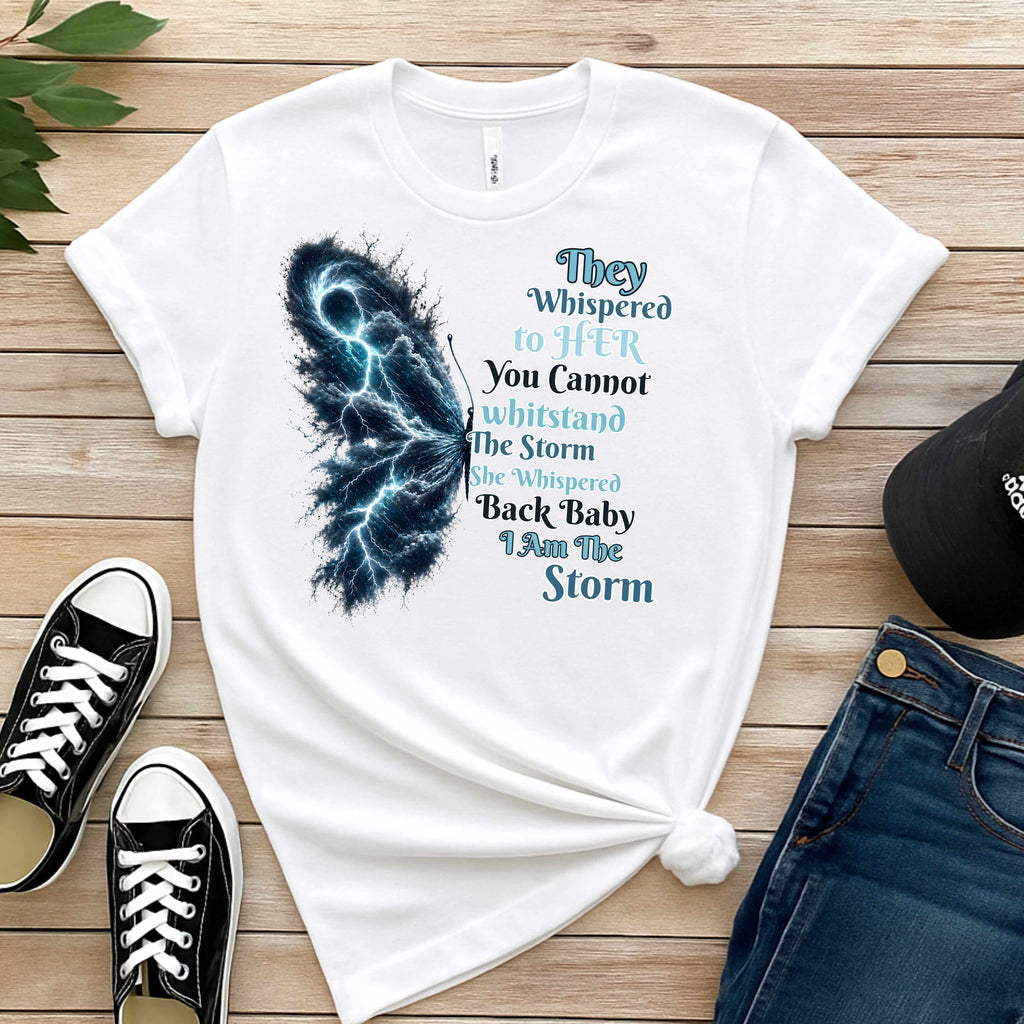 White t-shirt with a butterfly design and text on a wooden surface with shoes and jeans.
